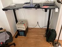 Side view of black electric adjustable desk with digital control panel, showing sturdy metal legs and desktop surface.
