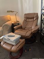 Brown faux leather recliner chair with matching footstool and a few other surrounding furniture pieces and accessories