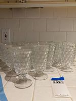 Photo showing multiple clear glass tall stemware glasses with diamond-patterned texture, arranged in rows on a countertop.