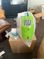 Oxygen concentrator on top of cardboard box with green tubing and small white accessory box visible next to it