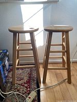 Pair of wooden bar stools in front of a window on a wood floor, showing overall look and style.