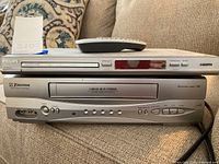Front and top view of Philips HDMI DVD player stacked on Emerson VHS player with remote on top, showing the front controls and disc tray.