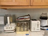 Overview of the lot showing KitchenAid food processor, metal rotary cheese grater, Cuisinart toaster, and Nostalgia popcorn maker.