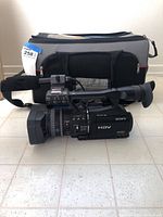 Side view of Sony HVR-V1U camcorder in front of gray and black carrying case