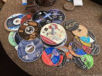 Photo of diverse video game discs spread on a carpet, featuring Star Wars, Warcraft, and Jak and Daxter among others.