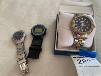 Three watches shown together: Invicta watch in box, digital compass watch, and small analog stainless steel watch