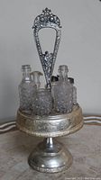 Full view of the Victorian silverplated castor cruet with intricate cherub handle and six glass bottles on the lazy Susan base