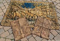 Large antique tapestry rug with deer and buck scene laid out, with two smaller French Victorian tapestries placed on top folded slightly.