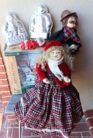 Two tall Victorian themed caroler dolls, one female and one male, displayed on a floor with a Department 56 box, fabric mouse figure, and metal Santa molds.
