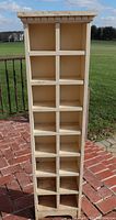 Full front view of the tall narrow wooden cabinet with chippy cream paint and multiple square cubby compartments. Displays overall condition and structure.