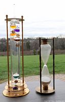 Photo of Galileo thermometer and hourglass sand timer shown outdoors with a grassy field background