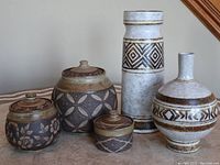 Five pottery items arranged on a table including two vases and three lidded canisters with geometric and floral patterns