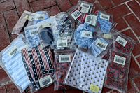 Photo of multiple Longaberger liners and handle ties, including American flag-starred fabric and blue-toned patterned items, all individually bagged with Longaberger tags.