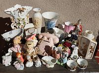 Wide view of entire porcelain lot with figurines, vases, and decorative pieces arranged on table against wall.