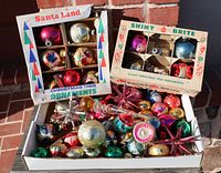 Wide view of assortment of vintage glass Christmas ornaments, including two boxed sets and loose ornaments in a white box. Visible are shiny round balls, starburst shapes, and candy cane ornament.