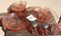 Lot includes various pink Depression glass pieces such as footed bowl, console plate, Honey Bear shakers on wooden table in sunlight.