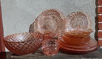 Wide view of assortment of pink Depression glass pieces including bowls, plates, and serving dishes displayed outdoors against wall.