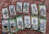 14 Lord of the Rings action figures in packaging laid out on brick ground. Includes characters Eowyn, Eomer, Frodo, and others. All original sealed packages showing character images and figure details.