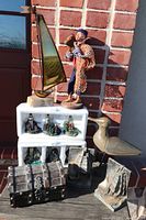 Photo showing the lot arranged with cast sailboat bookends, fisherman figure, wooden seagull, lighthouse ornaments, wooden treasure chest, and brass/marble sailboat sculpture on a porch against a brick wall.