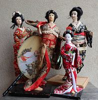 Four vintage Geisha dolls and one decorative fan grouped together showing attire, size, and condition.