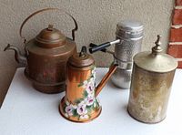 Four vintage kitchen items displayed on white table: copper tea kettle with lid, hand painted copper coffee pot, hammered aluminum coffee pot with black handle, brass sugar canister with etched lid.