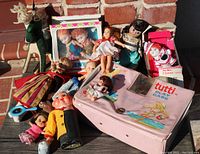 Pink Tutti play case surrounded by several vintage dolls including Pee Wee Clown, Madame Alexander style doll, and some doll clothing.