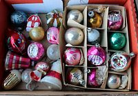 Top view of open box containing various vintage glass ornaments of different shapes, colors, and styles packed loosely in a cardboard box