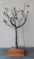 Metal wire tree sculpture with branches, leaves, and hanging metal swing on wooden base