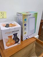 Photo showing the boxed aroma diffuser and Verilux HappyLight energy lamp side by side on a wooden surface.