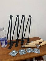 Four 12-inch black metal hairpin legs standing upright and four 6-inch wooden legs lying on surface with mounting hardware.