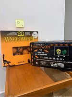 Shows two boxed Halloween light sets, one labeled Danson Inc. with 20 blinking pumpkin lights, and the other labeled Afterbrook Halloween with 10 light pieces featuring pumpkin, skull, and zombie designs.