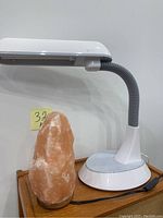 Photo showing Himalayan salt lamp with natural pink-orange salt body on wooden base, next to white OttLight adjustable desk lamp with flexible neck and weighted base.