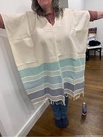 Front view of handwoven poncho worn by model, showing cream color with blue and grey stripes and fringe detail