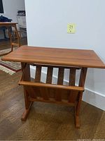 Front view of solid teak magazine table showing flat top surface and slatted compartments with a center divider.