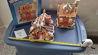 Two porcelain holiday houses side by side. The M&M candy house with colorful M&M candy decorations sits near a PartyLite candy house candle holder. A tape measure shows approximately 8.5 inches tall.