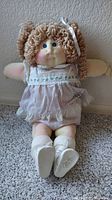 Full front view of Cabbage Patch Kid doll sitting upright on carpet, showing facial features, hair, outfit, socks, and shoes.