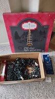 Red box labeled 'Trim A Home 250 clear light spiral tree' with cardboard box containing green wired Christmas lights and a blue box of icicle lights next to it.