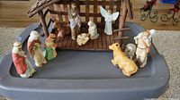 Wide view of entire 12 piece ceramic Nativity set arranged with manger stable, human figures, and animals.