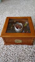 Top view of the closed wooden music box showing glass display and brass Santa's Workshop plaque.