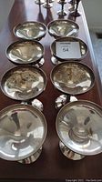 Top angled view showing eight silver plated dessert cups arranged in two rows on a wooden surface, with visible tarnish and reflective surfaces.
