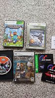 Photo showing Minecraft and Ace Combat 6 Xbox 360 game cases, Sims 3 disc, Treasures of Mystery case, and Gran Turismo manual and case.