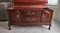 Exterior front view of large wooden cedar chest showing two drawers with brass handles and two cupboard doors with brass keyhole escutcheons, ornate carved legs and apron