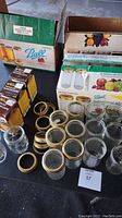 Photo of various glass jelly jars and metal lids, including boxes from Ball brand with some boxes showing new lids and jars.
