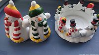 Photo of two ceramic snowman-shaped pillar candle holders, one with red scarf and hat, the other with green scarf and hat.