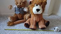 Photo of two seated stuffed animals, lion in front and bear in background with measuring tape for size reference.