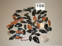 Photo of a spread lot of 44 varied arrowheads in black, rusty red, and beige hues on a neutral surface.