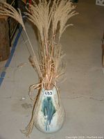 Full view of the clay pottery vase standing on the floor, filled with dried grass