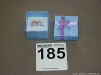 Image of ring in blue gift box with purple ribbon, displayed with auction lot number card