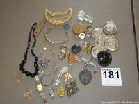 Photo of full lot showing various necklaces, charms, a wristwatch, brass pieces, and children's police badges laid out on a table