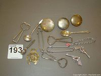 Photo of assorted small metal items including keychains, small spoons, and bottle openers laid out on a beige surface.